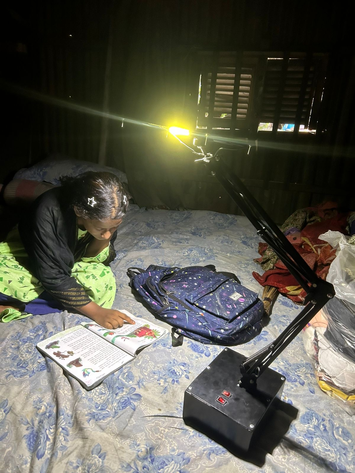 Child reading in bed with adjustable LED lamp; portable battery visible.